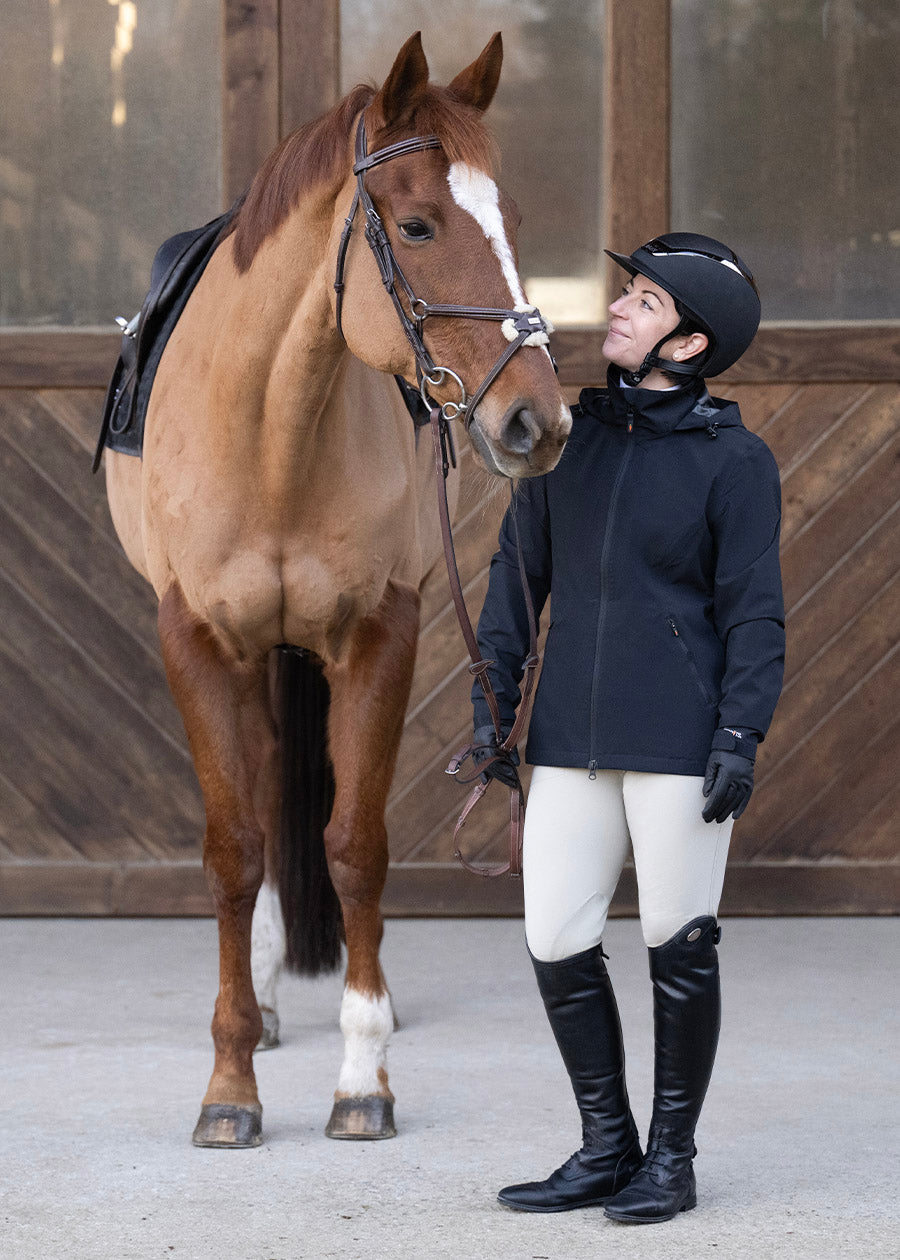 Model standing with horse wearing the Waterproof All Around Rain Jacket showing the sleek design and full-length sleeves