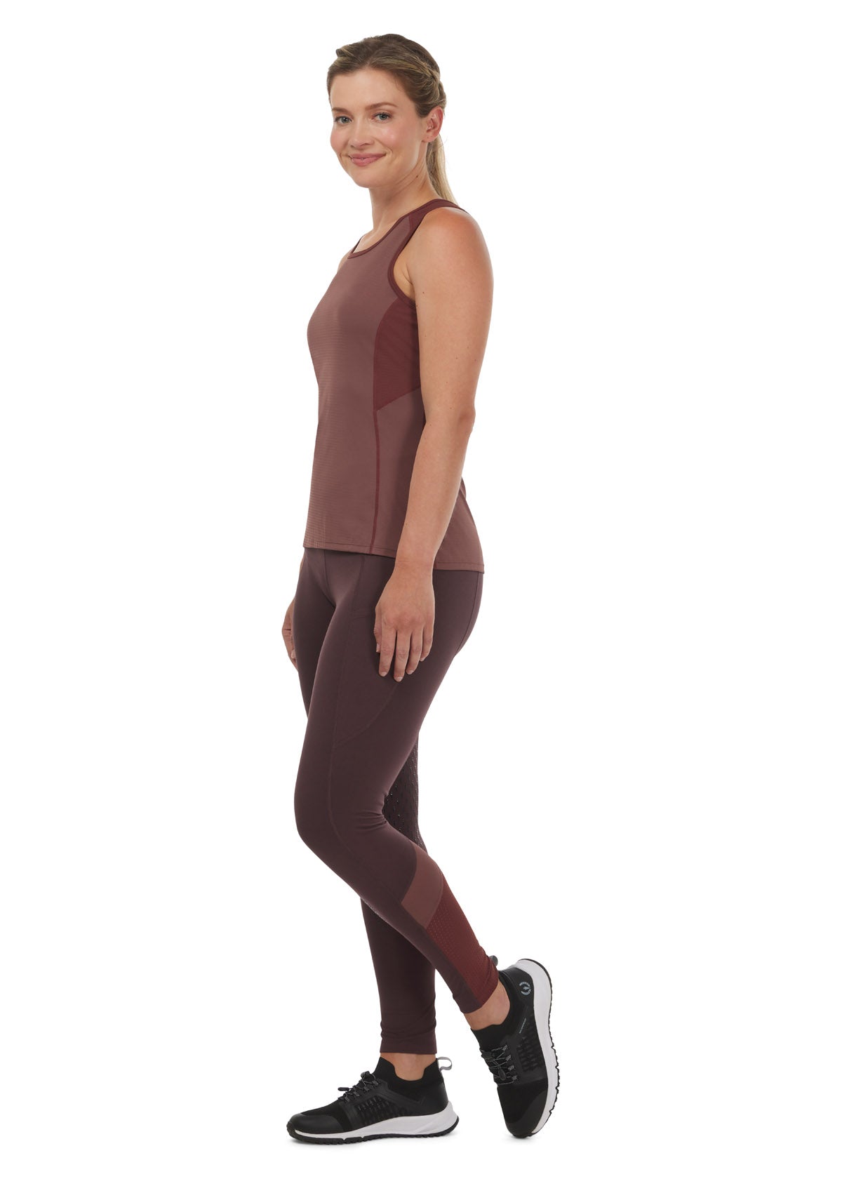 Model wearing the Kerrits Freedom Tech Riding Tank Top in Sedona, paired with a burgundy pair of riding tights for a sporty casual equestrian look.