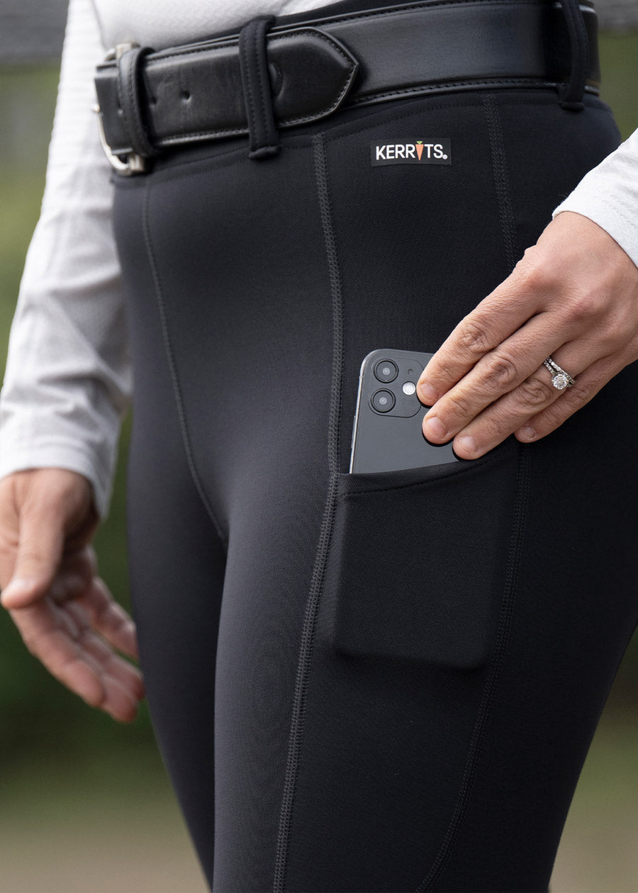Close-up of a rider putting their phone in their pocket on the Flex Lite Knee Patch Riding Tight.