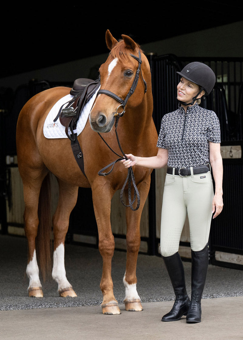 Rider wearing the Kerrits K-Flex™ Knee Patch Breech while walking through the barn aisle, showing its polished and professional look.