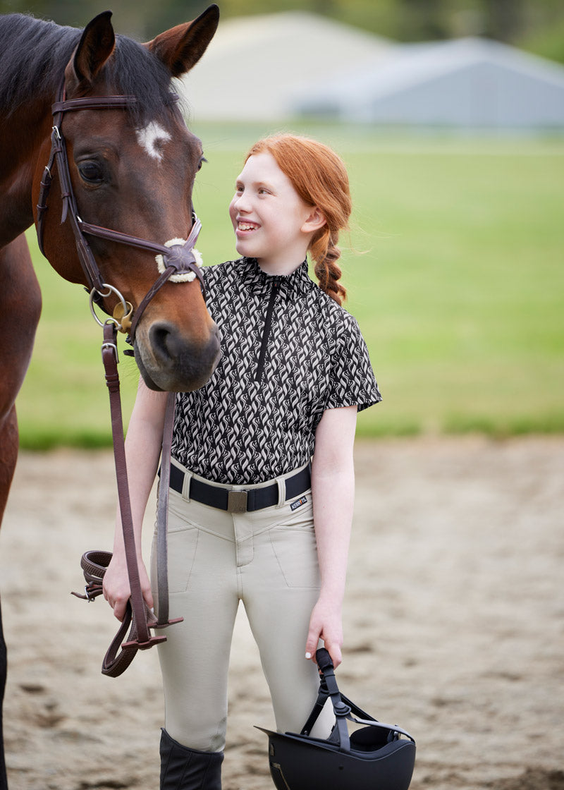 Rider standing beside a horse, dressed in the Crossover II® Knee Patch Breech, highlighting the stylish and functional design suitable for competitions
