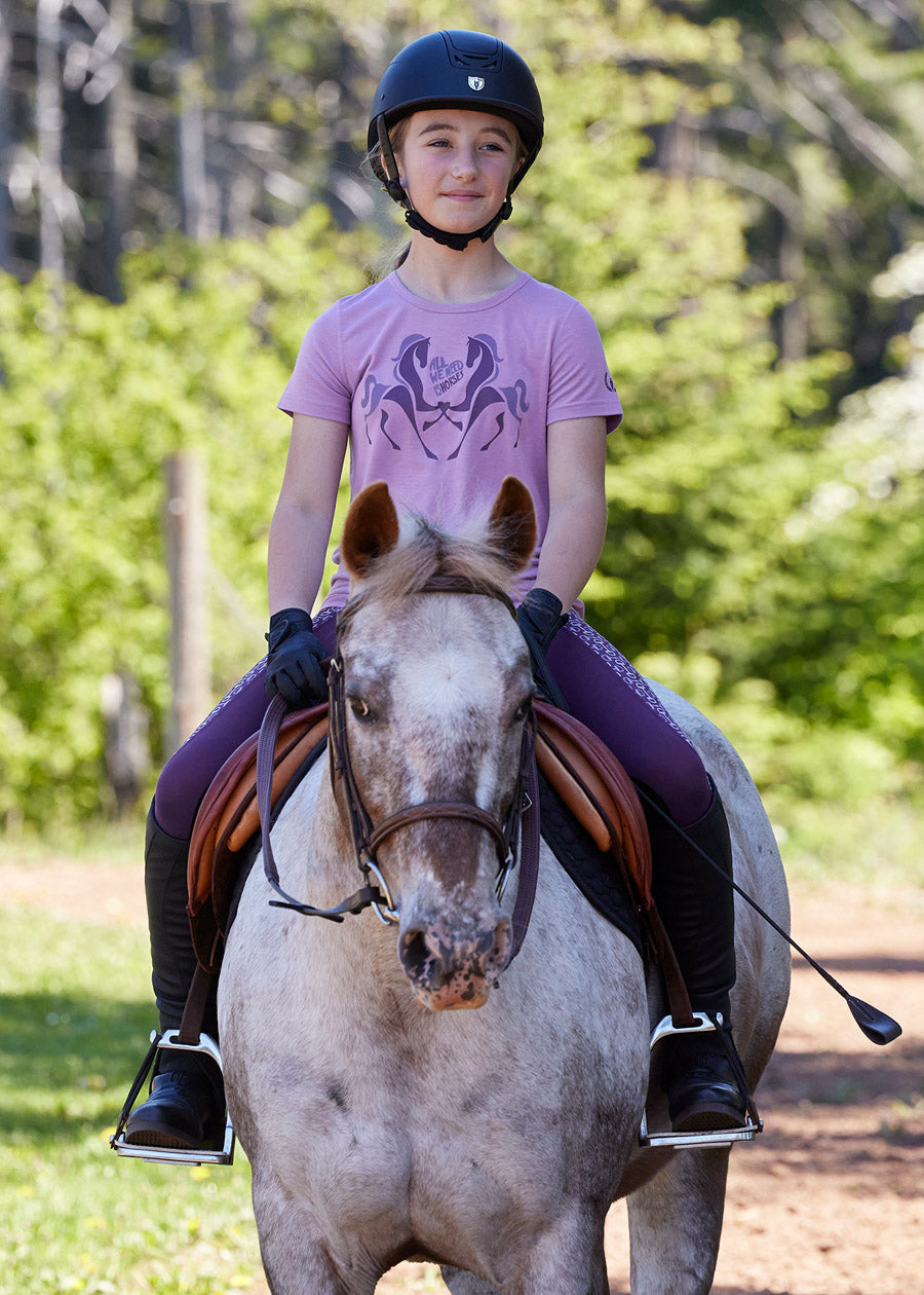 Young rider wearing the All We Need Is Horses Tee while grooming a horse, demonstrating the tee's comfort and equestrian appeal