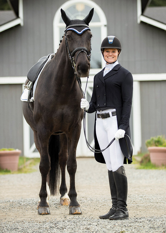 Rider wearing the black Affinity® Aero Shadbelly Show Coat outside an arena, paired with a horse, exemplifying professional show attire.