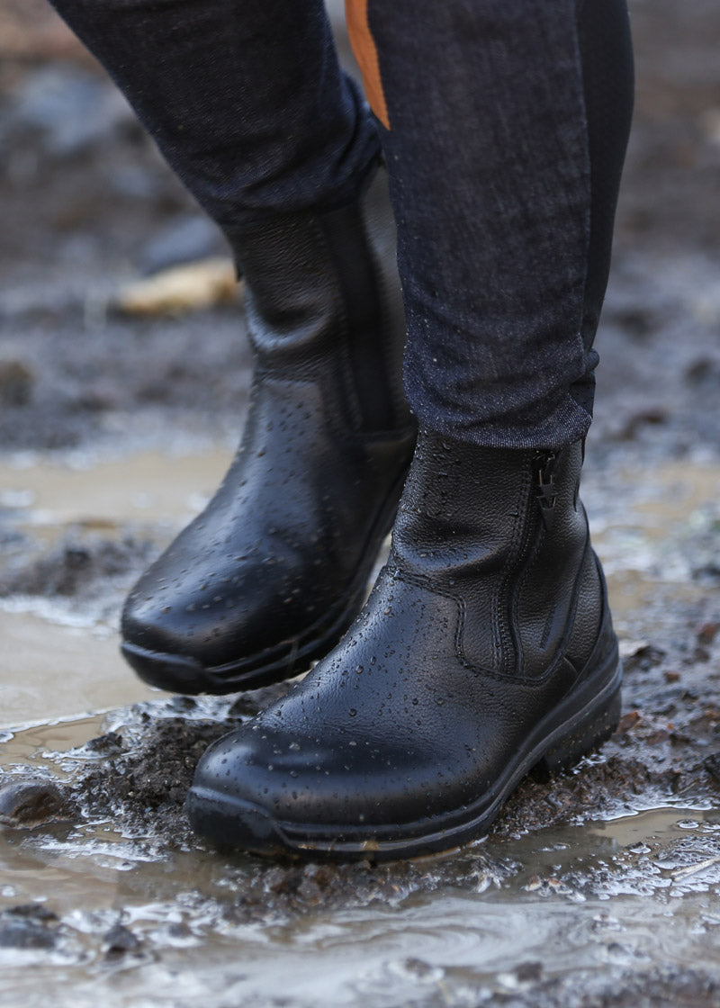 Individual walking through wet barnyard in Woodstock Waterproof Barn Boot, illustrating waterproof feature and non-slip traction
