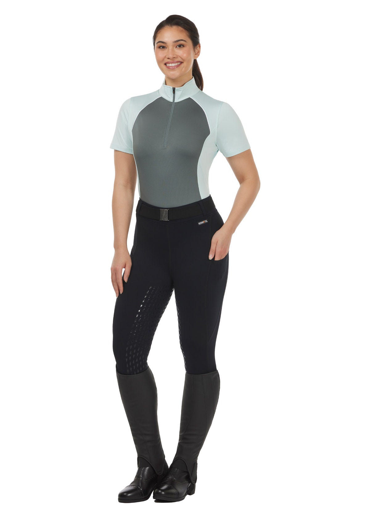 Model wearing the Charisma Coolcore Short Sleeve Riding Shirt in Sagestone, styled with black riding tights for a functional summer riding outfit.