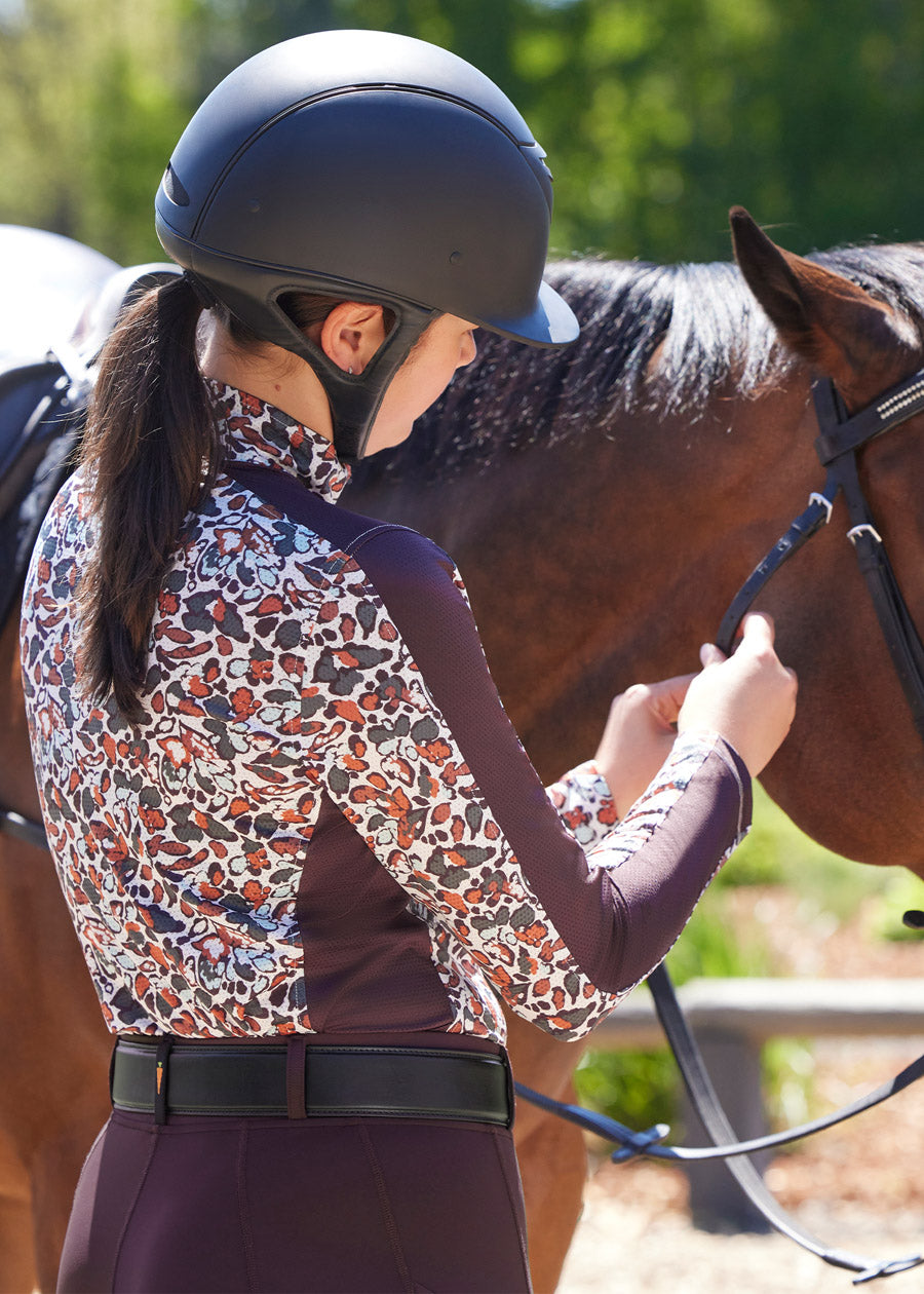 Back view of the Breeze Ice Fil® Long Sleeve Riding Shirt worn by a rider, highlighting the equestrian-inspired print and sporty details