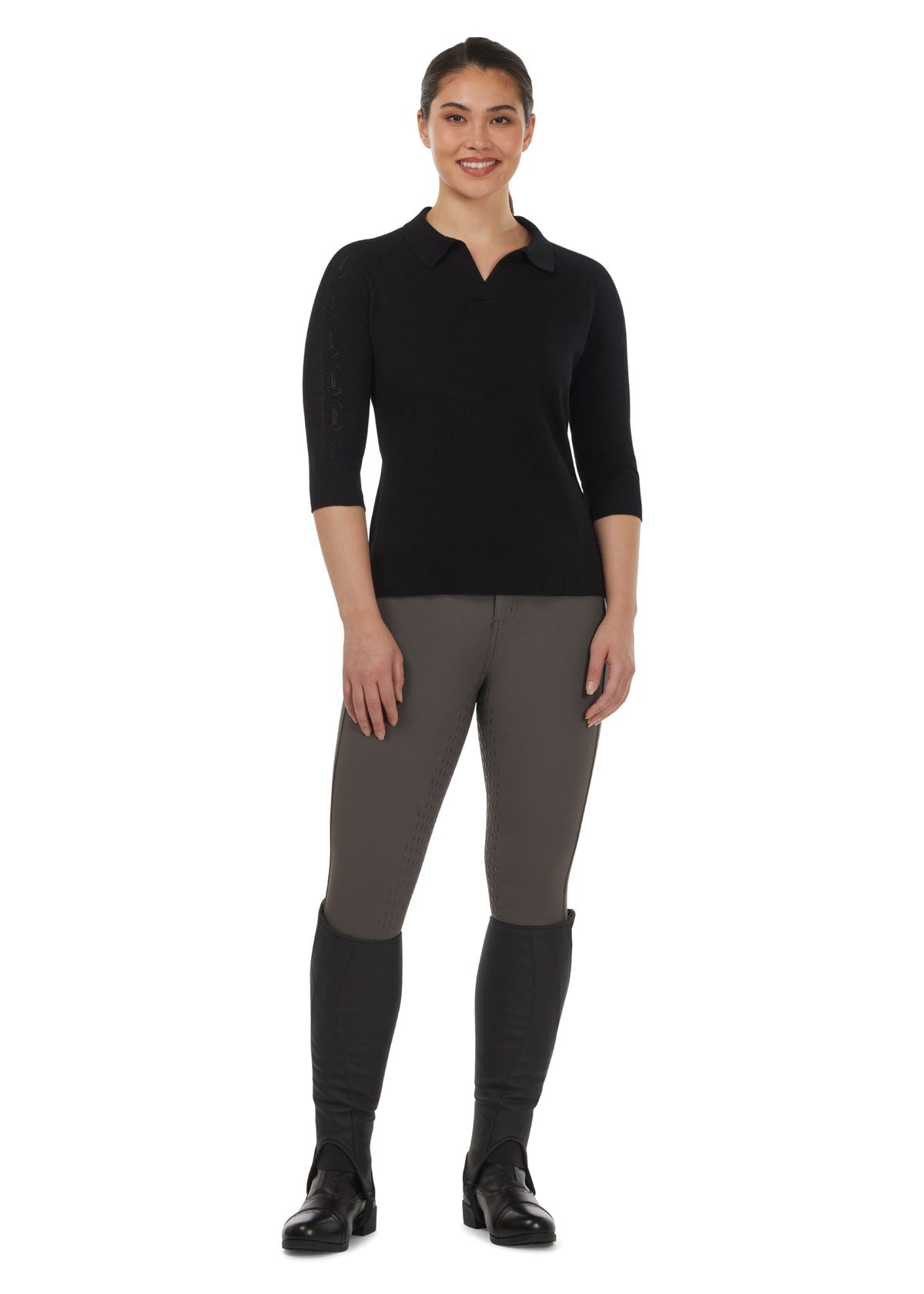 Model wearing the Bit of Breeze Sweater Knit Polo in Black, paired with breeches for a casual yet stylish equestrian outfit.